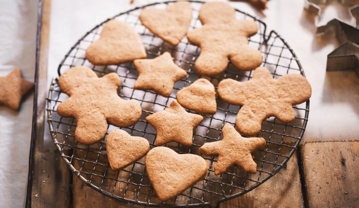 Em cima de uma mesa, grade com biscoitos em formato de coração, estrelas e bonecos de gengibre.