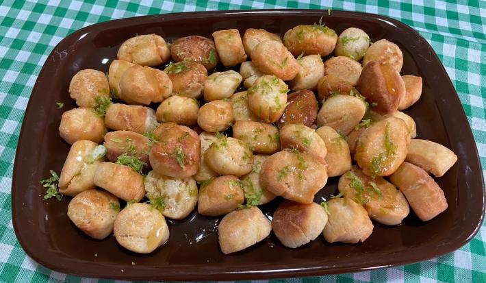 Foto aproximada da receita de pinholate de natal, bolinhas pequenas e crocantes, servidas todas em uma travessa marrom, cobertas com mel e raspas de limão