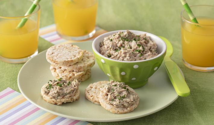 Foto da receita de Pate de Sardinha. Observa-se uma cumbuca verde clara com o patê dentro e, ao lado, biscoitos de arroz servidos com a receita.