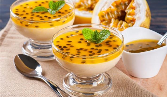 Imagem de duas taças de mousse de maracujá decoradas com sementes de maracujá e folhas de hortelã. Ao lado, duas partes de maracujá ao meio.