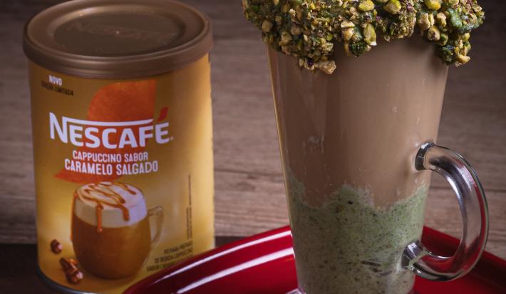 Foto da receita de cappuccino de pistache servida em um copo alto de vidro sobre uma mesa de madeira