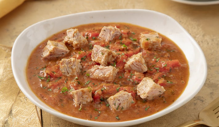 Goulash moderno de atum servido em prato fundo, com cubos de peixe em molho de tomate encorpado e ervas frescas.