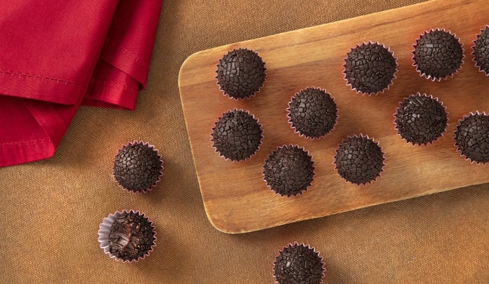Fotografia vista de cima de vários brigadeiros de nescau enrolados e passados no granulado, dentro das forminhas vermelhas de papel.