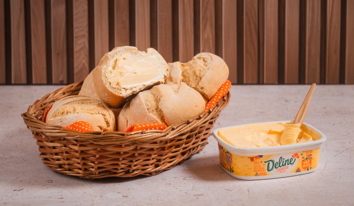 Pãezinhos de milho caseiros em cesta com margarina Deline derretendo em um pão