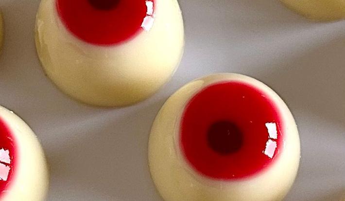 Fotografia em tons claros de varios olhos de gelatina e leite moça para o halloween sobre uma mesa branca.