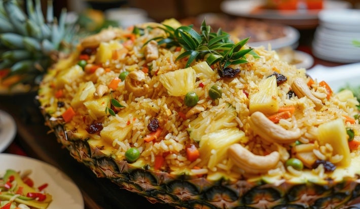 Em um abacaxi cortado ao meio, porção de arroz com abacaxi picados, ervilhas, cenouras em cubos e castanha-do-Pará.