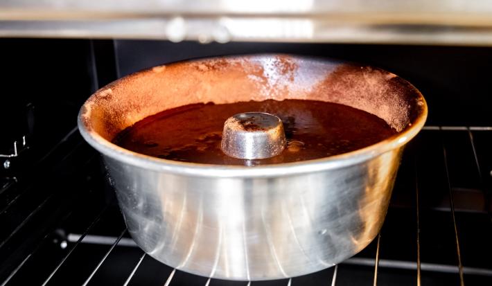 Foto aproximada de uma forma de alumínio de furo central com a massa do bolo dentro. Ela está dentro de um forno.