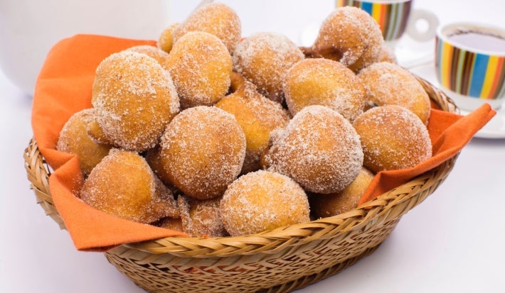 Em cima de uma mesa, cesta de palha com pano laranja com bolinhos de chuva, polvilhado com açúcar de confeiteiro.