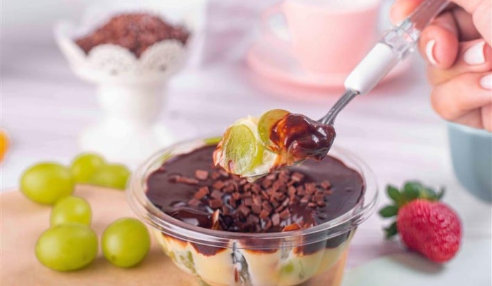 Fotografia em tons de verde com uma taça de vidro ao meio com sobremesa de chocolate e uva dentro.