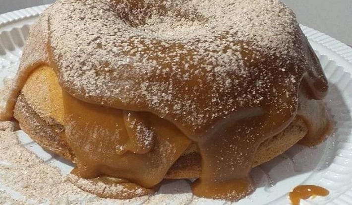 Foto em tons de marrom da receita de bolo vulcão de churros com bastante cobertura de doce de leite com canela salpicada por cima
