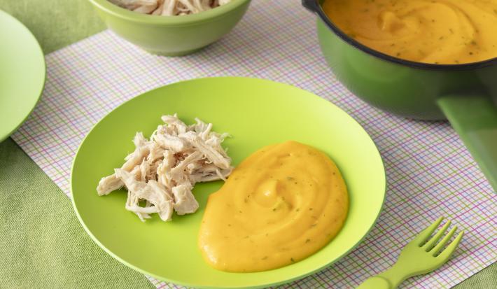 Foto da receita de pure de batate e cenoura. Observa-se um prato verde bebê com o purêzinho laranja do lado direito e um franguinho desfiado do lado esquerdo.
