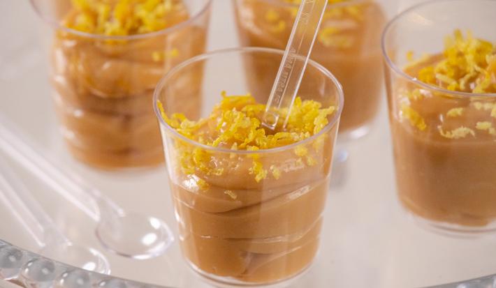 Fotografia em tons de branco com vários potinhos de plástico ao centro. Dentro de cada potinho existe uma receita de brigadeiro de colher de limão siciliano, finalizado com raspas de limão siciliano.