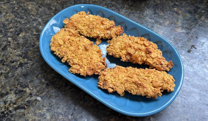 Fotografia mostra quatro filés de frango empanados, com textura crocante e dourada sobre um prato azul.