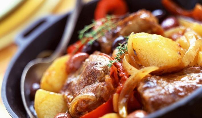 Fotografia em tons de vermelhos, em uma bancada de madeira de cor branca. Ao centro, um pano amarelo dobrado com um recipiente em cima contendo o bife e ao lado, há uma colher.