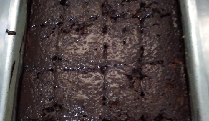 Foto da receita de Bolo de Chocolate. Observa-se um tabuleiro com bolo de chocolate com calda por cima cortados em formatos retangulares