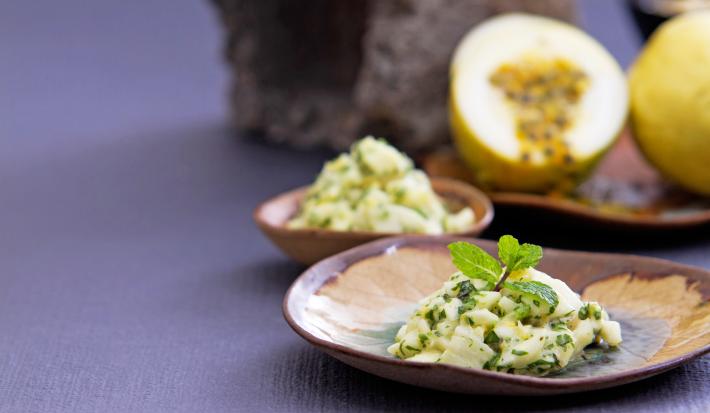 Foto da receita de salada de casca de maracujá, servida sobre um prato em formato de folha de árvore, numa bancada com um maracujá aberto ao fundo