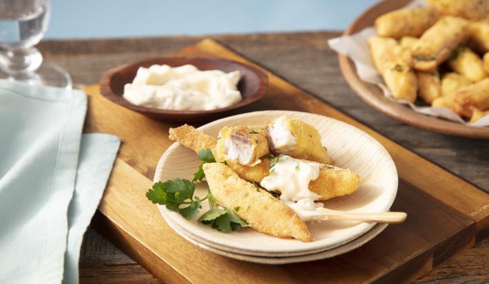 Imagem de um prato com iscas de tilápia frita e molho. Ao fundo, um bowl com iscas de tilápia e um potinho com molho.