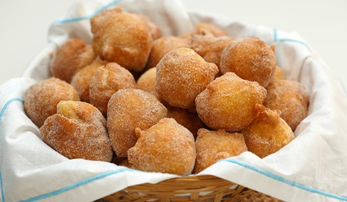 Fotografia em tons de branco de uma  bancada branca com uma cesta, sobre ela um paninho branco com bolinhos de chuvas.