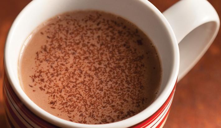 fotografia em tons de marrom e branco tirada de cima, contém uma xicara com chocolate quente.