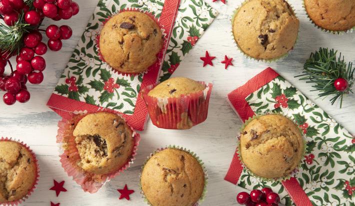 Foto da Receita de Muffin Natalino feito na Air Fryer. Observa-se 7 muffins de baunilha com chocolate em forminhas natalinas vistos de cima. Decorações natalinas enfeitam a foto, como guardanapos e decorações de árvore de Natal.