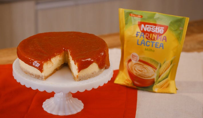 imagem mostra uma cheesecake cremosa de milho com cobertura de goiabada em uma forma redonda.