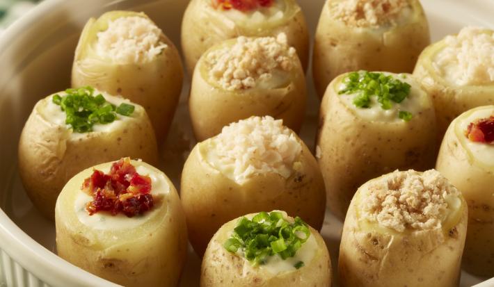 foto em tons de amarelo, verde e branco tirada de uma recipiente redondo branco com mini batatas recheadas. Abaixo um pano xadrez em tons de verde e branco.