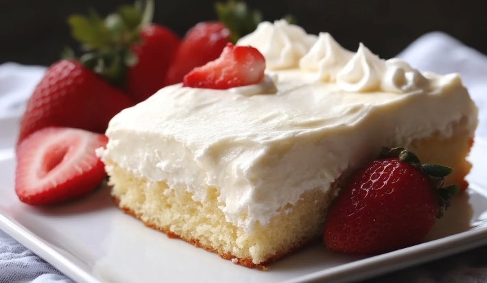 Em cima de uma mesa, prato branco com pedaço de bolo com massa branca, creme branco e morangos cortados ao meio.