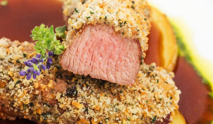 Fotografia de uma fatia de carne cortada pela metade e mostrando seu interior avermelhado. Por fora da carne, observa-se uma crosta dourada com pequenos pontos de tempero.