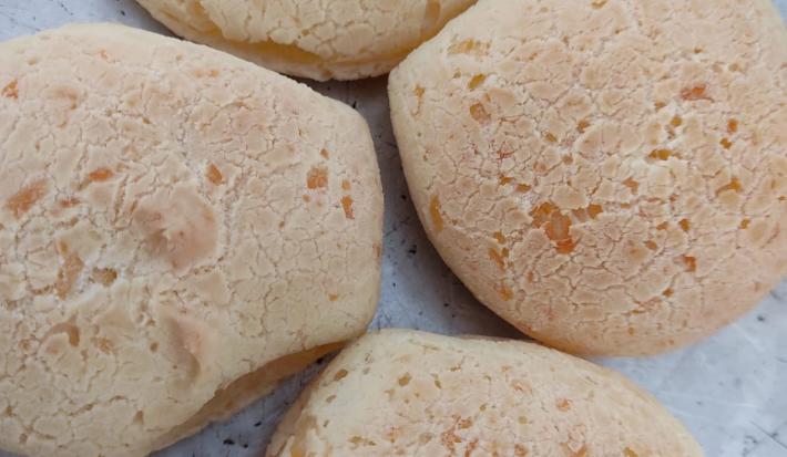 Fotografia de quatro pães de queijo sobre uma forma de alumínio.