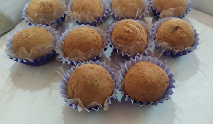 Fotografia em tons de marrom em uma bancada branca e docinhos de cacau dentro em forminhas azuis