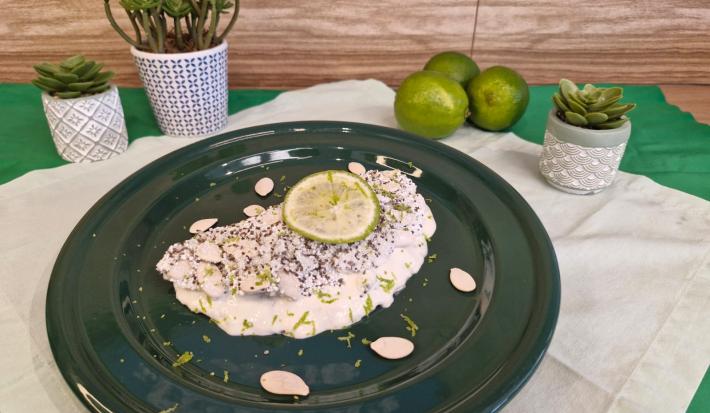 Foto em tons de branco da receita de tapioca servida com uma rodela de limão por cima, sobre um prato preto em cima de uma toalha de linho com limões e vasinhos de planta ao lado