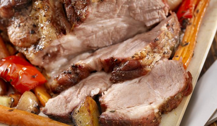 Fotografia em tons de marrom tirada de um pernil com diversas fatias à frente.