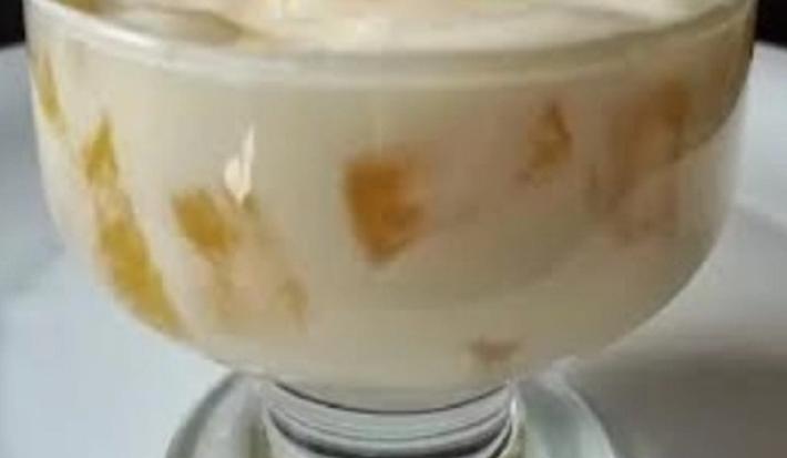 Foto da receita de mousse de abacaxi servida em uma taça de vidro com pedaços de abacaxi à mostra sobre um prato de porcelana branco