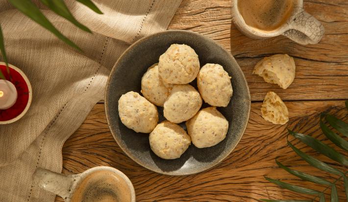 Foto da receita de pão de queijo de aveia servida em diversas porções em um bowl de cerâmica cinza em cima de uma mesa de madeira com um pano de linho ao lado