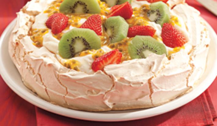 Fotografia em tons de vermelho de uma bancada com um pano vermelho sobre ele um prato branco com Pavlova. Ao fundo uma colher.