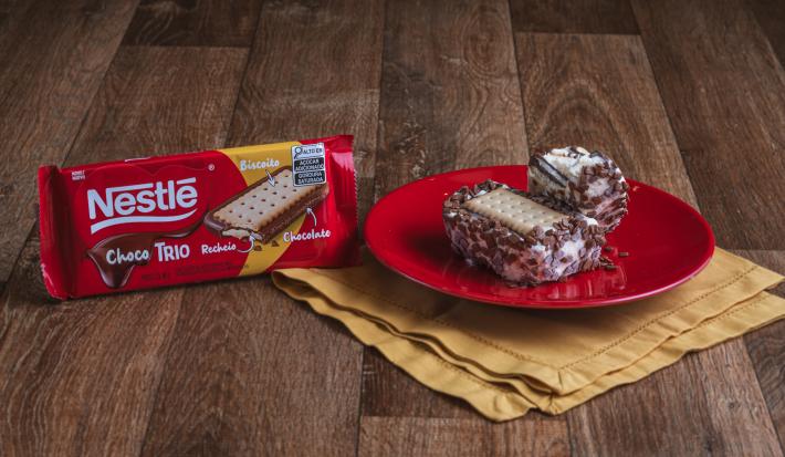 Foto da Receita de Sanduíche de Sorvete com Choco Trio. Observa-se dois sanduíches (um inteiro e um mordido) sobre um prato vermelho redondo e pequeno e, ao lado, a embalagem de ChocoTrio
