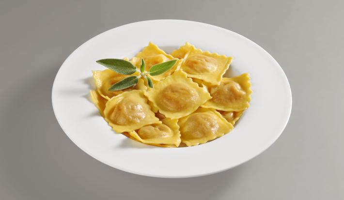 Foto da receita de Tortelli. Observa-se um prato repleto de tortellis com sálvia em um prato branco redondo.