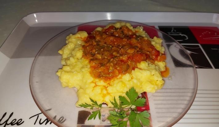 Fotografia de um prato raso transparente com uma polenta caseira. Por cima tem molho de tomate e, ao lado, tem salsinha.