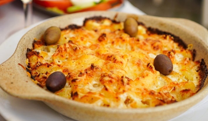 Em cima de uma mesa, refratário redondo com bacalhau gratinado com queijo, decorado com azeitonas pretas e verdes.