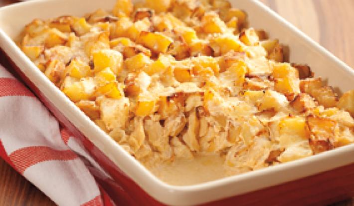 Fotografia em tons de vermelho e amarelo de uma bancada de madeira com um pano quadriculado branco e vermelho, uma travessa retangular vermelha por fora e bege por dentro com o bacalhau gratinado com cubos de batata por cima, faltando uma porção.
