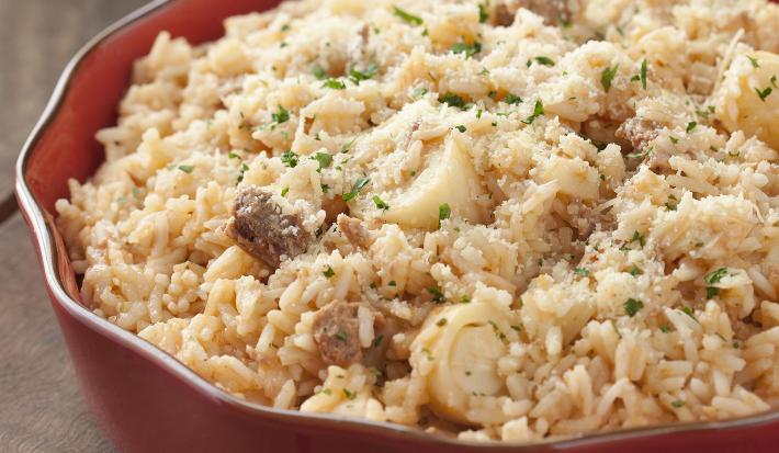 fotografia em tons de cinza e vermelho de uma bancada cinza vista de cima. Contém um recipiente vermelho redondo com o risoto e ao lado um pano vermelho