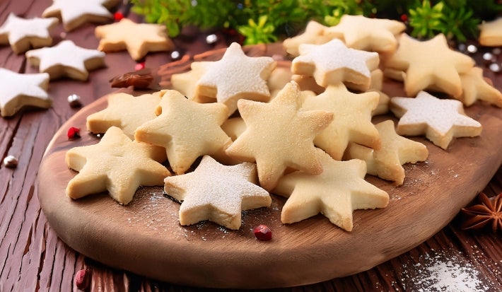 Em cima de uma mesa, prato com biscoitos em formato de estrelas, polvilhados com açúcar de confeiteiro.