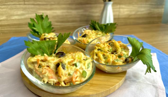Fotografia em tons de azul com uma tábua de madeira ao centro. Em cima da tábua existe 4 potinhos de vidro. Dentro de cada pote existe uma receita de salpicão de frango com cenoura, uva passa e ASCENDA