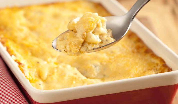 fotografia em tons de marrom, vermelho, amarelo e branco tirada de uma tábua de madeira, por cima um recipiente retangular vermelho e branco com a batata gratinada dentro.