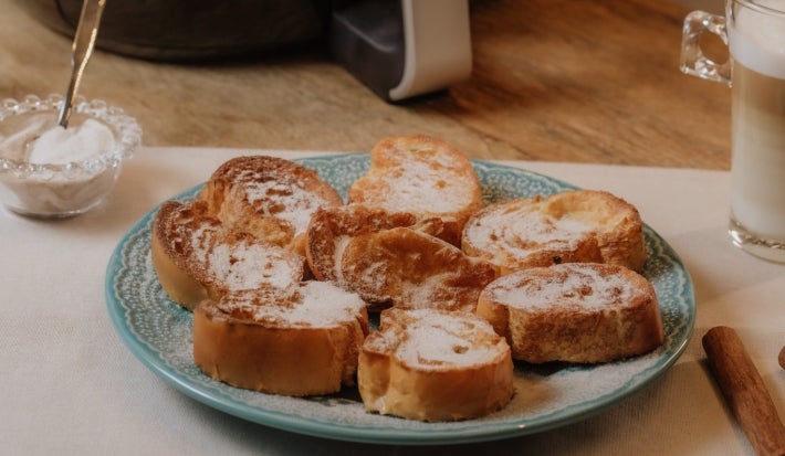 Prato azul com fatias de rabanada polvilhadas com açúcar e canela e uma air fryer no fundo.