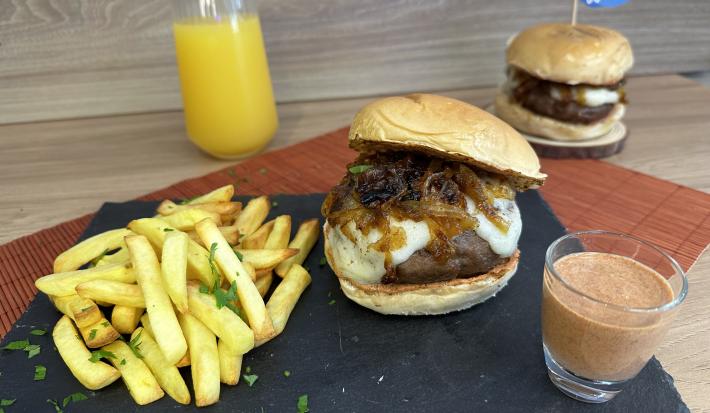 Fotografia de dois hambúrgueres acompanhados de uma porção de batatas fritas e um molho avermelhado.