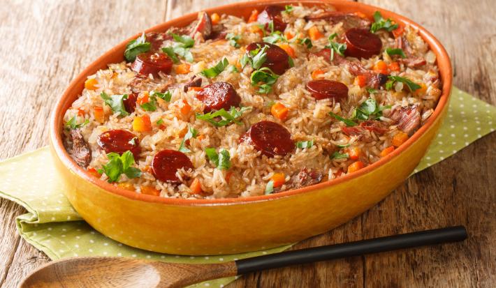 Fotografia mostra um arroz com pedaços de linguiça e temperos verdes dentro de uma travessa de servir.