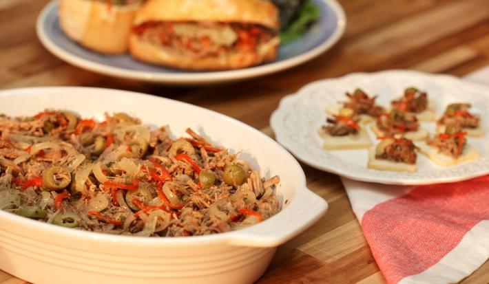 fotografia tirada de uma travessa branca com carne desfiada dentro com pedaços de azeitonas ao lado um prato redondo e branco com a carne desfiada e pedaços de azeitonas e abaixo um pano branco e vermelho