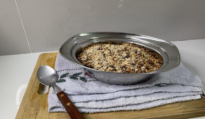 Imagem da receita de Farofa Proteica em uma vasilha de aluminio sobre uma toalha em uma mesa, ao lado uma colher