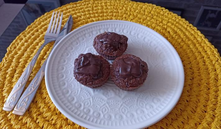 Imagem da receita de Muffin de cacau com coco e cobertura de chocolate meio amargo, em um prato branco, sobre uma mesa e ao lado os talheres